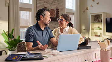 A photo of a couple in their 70s meeting with their financial professional at their kitchen table.