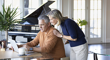 Another couple in their 70s, sitting at home on their sofa, looking together at a laptop computer.