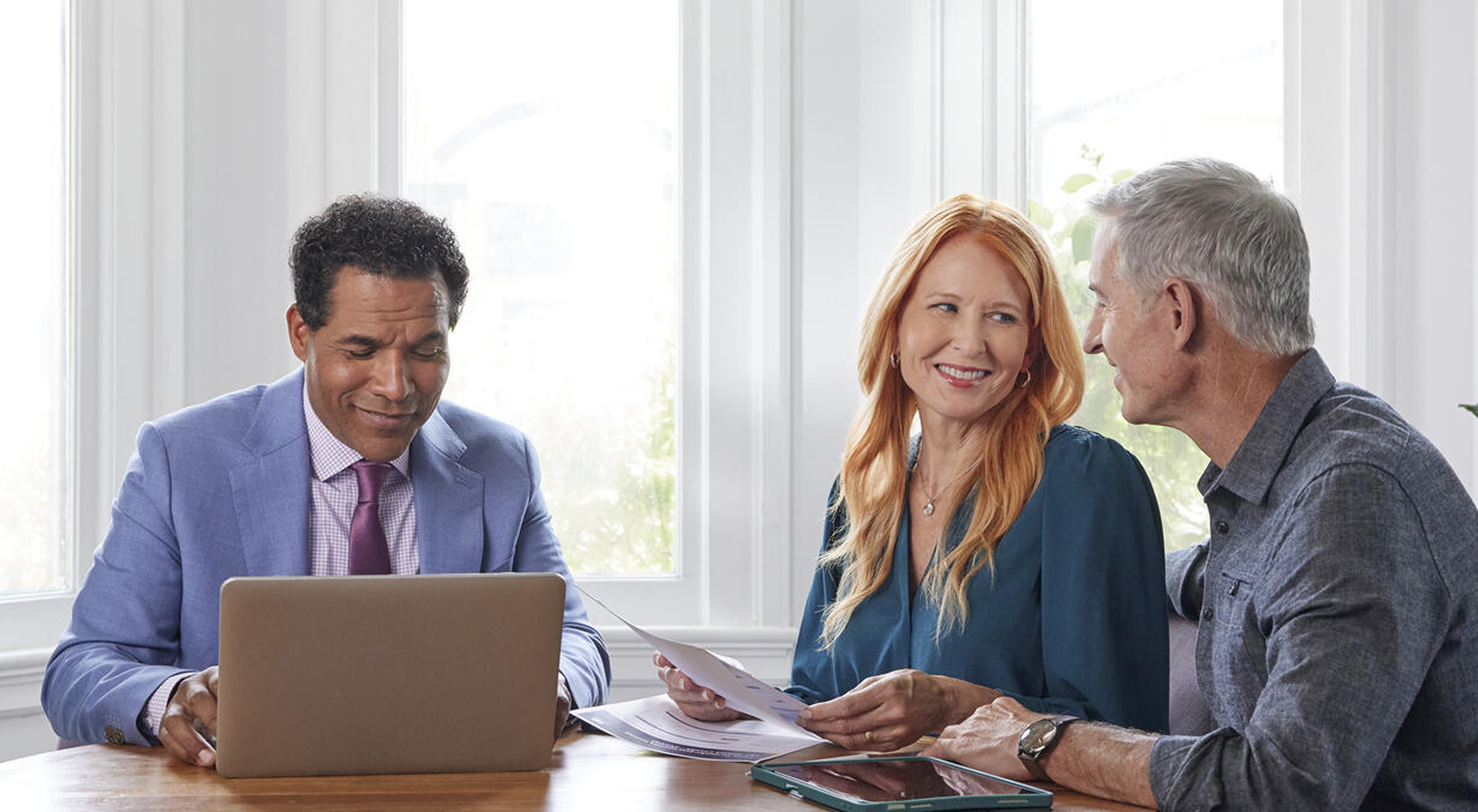a couple sitting a table talking with a man in a suit looking at a laptop