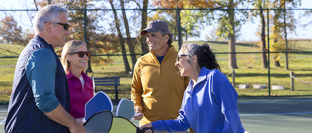 Two senior couples enjoying their retirement, socializing with each other and playing pickleball on a sunny autumn day.