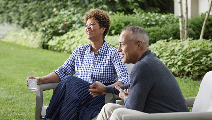 A middle aged married couple holds hands while relaxing in their backyard.