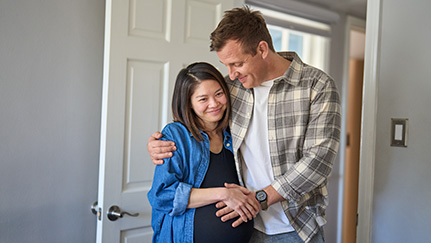 A happy, expecting couple hugging each other.